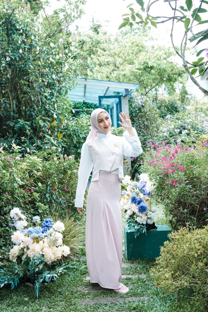 OOTD muslimah dengan vest asimetris krem dan rok panjang pink pastel di taman.