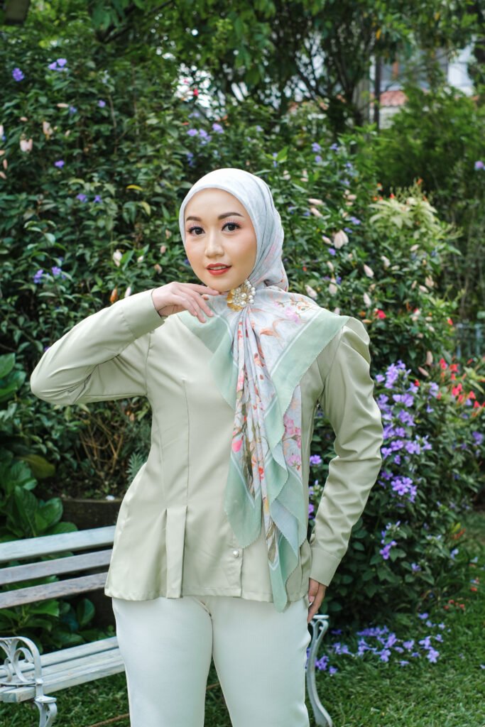 Potret wanita berhijab motif bunga mengenakan blus hijau sage dan bros mutiara.