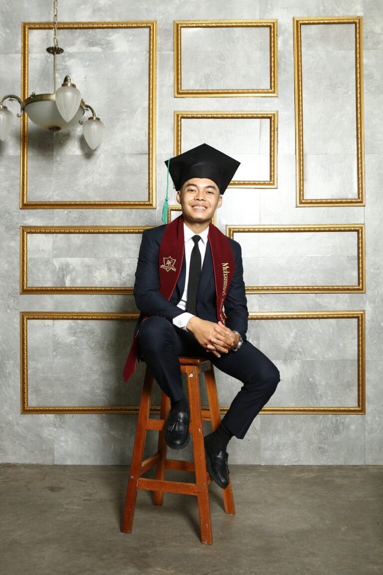 Wisudawan pria berpose di tangga mengenakan setelan jas biru elegan dan medali kelulusan.