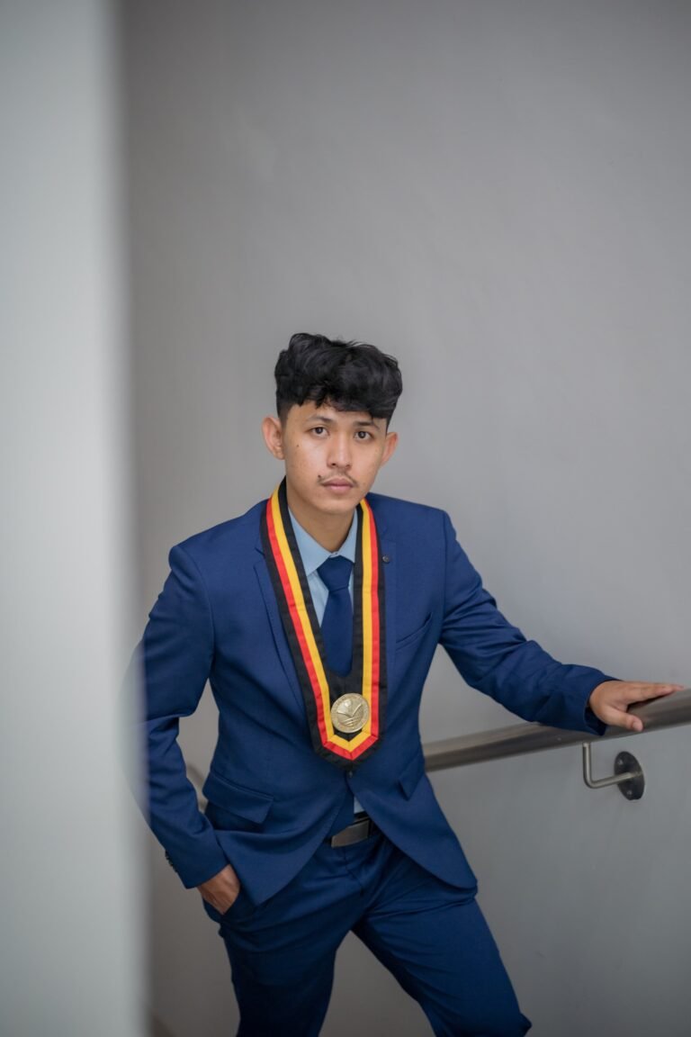 Pria wisudawan mengenakan jas biru custom dari Makaffah Signature dengan medali wisuda, berpose di tangga modern.