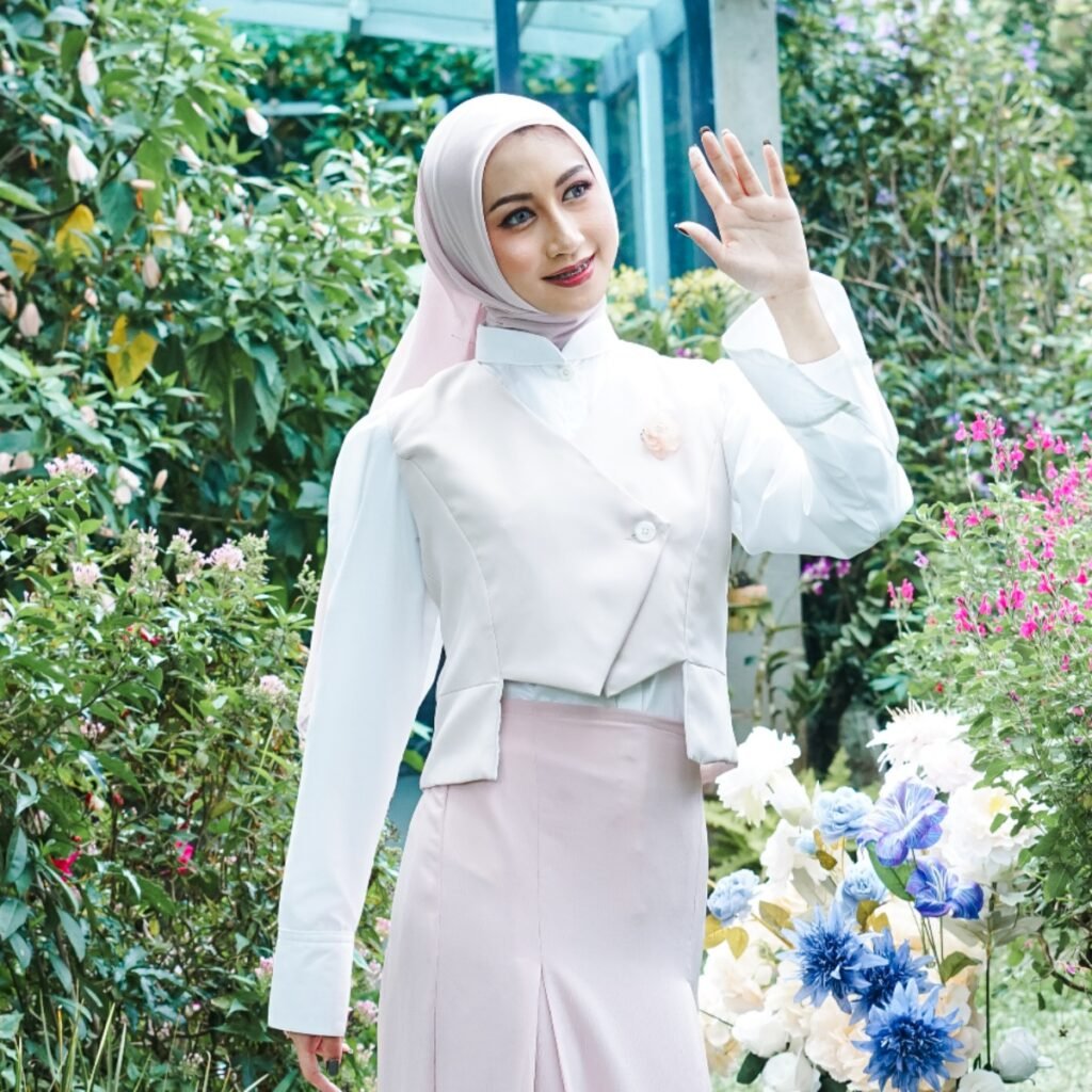 OOTD muslimah dengan vest asimetris krem dan rok panjang pink pastel di taman.